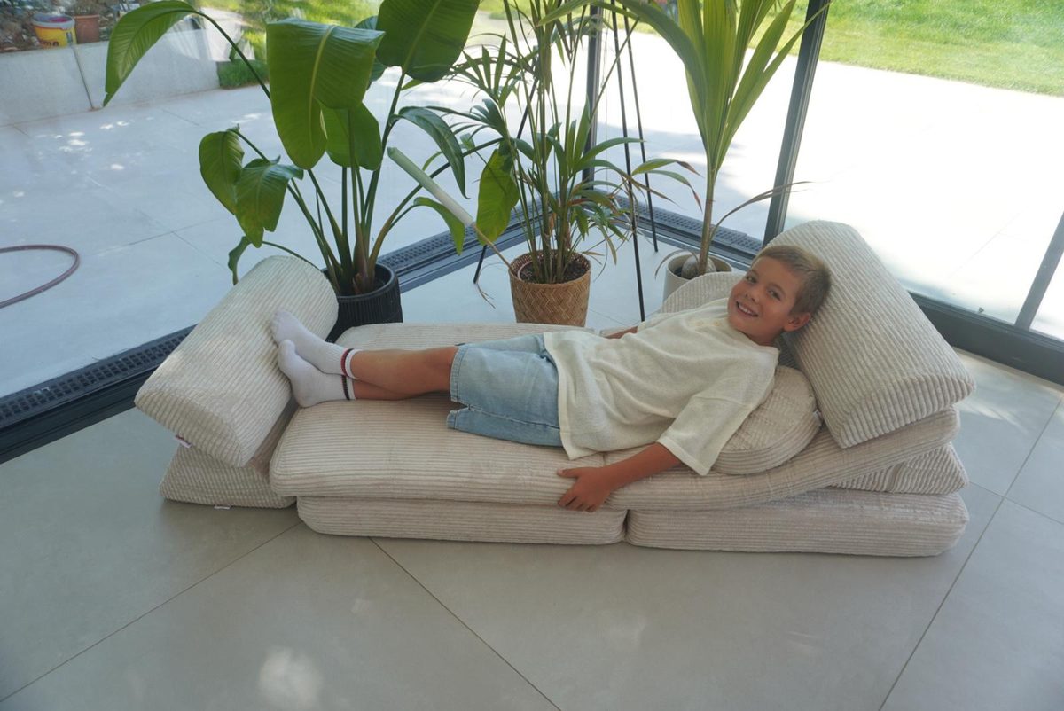 Kind liegt auf dem Linodino Spielsofa Fantasiewelt in Elfenzauber Beige, die beiden Armlehnen sind links und rechts angesetzt