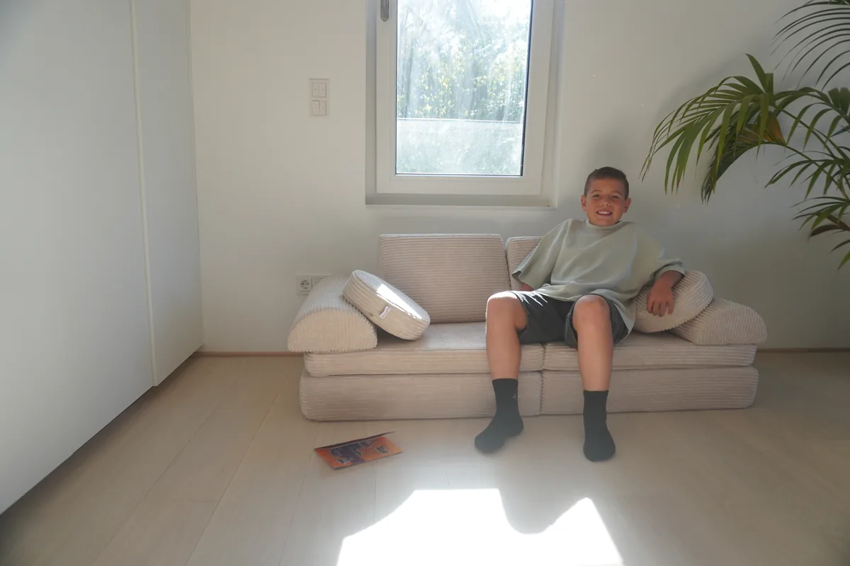 Kind sitzt lachend auf dem Linodino Spielsofa während unseres Praxistests